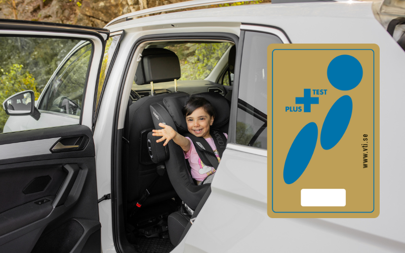 Girl sitting in car seat waving out the open car door, with a plustest symbol edited onto the picture. 